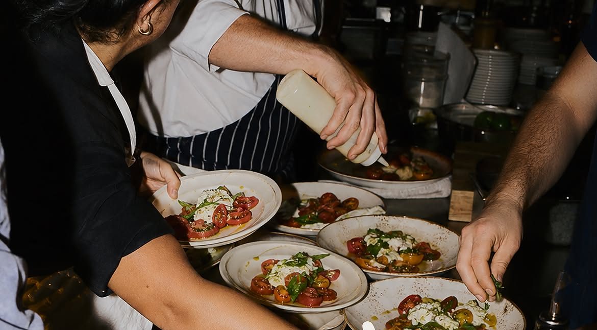 Plusieurs assiettes de tomates et burrata dressées au passe, à quatre mains